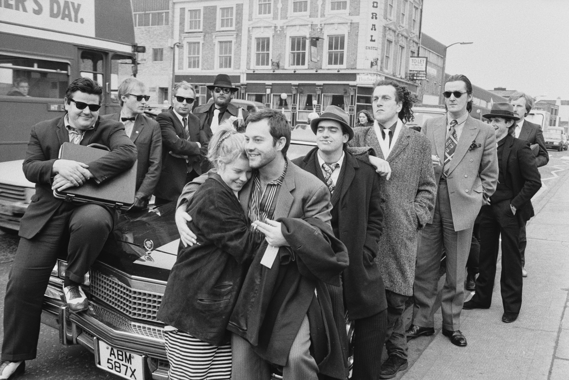 British film producer Alison Owen and her husband, British actor Keith Allen with cast members, British actors Robbie Coltrane, Adrian Edmondson, Peter Richardson, Kevin Allen and Clive Russell posing around Cadillac on the set of 'The Supergrass' outside Pentonville Prison on Caledonian Road in London, England, 24th January 1985. (Photo by D. Jones/Daily Express/Hulton Archive/Getty Images)