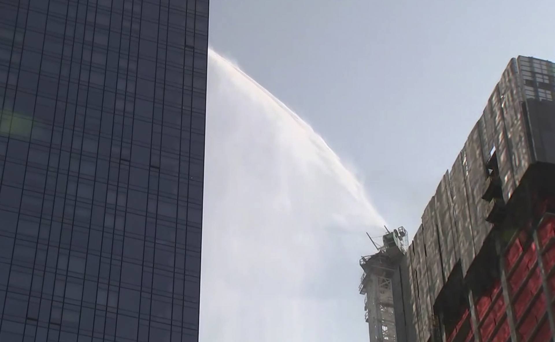 First responders spray water on tall construction crane that caught fire in Manhattan on Wednesday, July 26, 2023 in New York.  The crane caught fire and its arm hit a building as it crashed to the street below.  (WABC via AP)