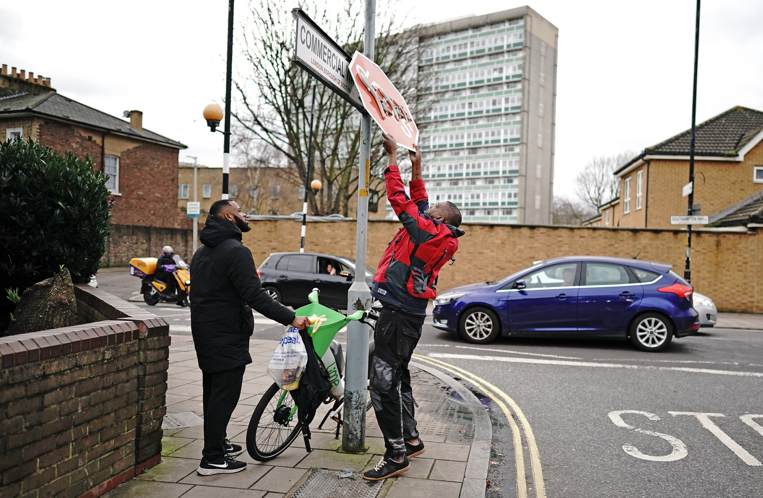 A man stands on a bike to remove a piece of art work by Banksy (Aaron Chown/PA) 