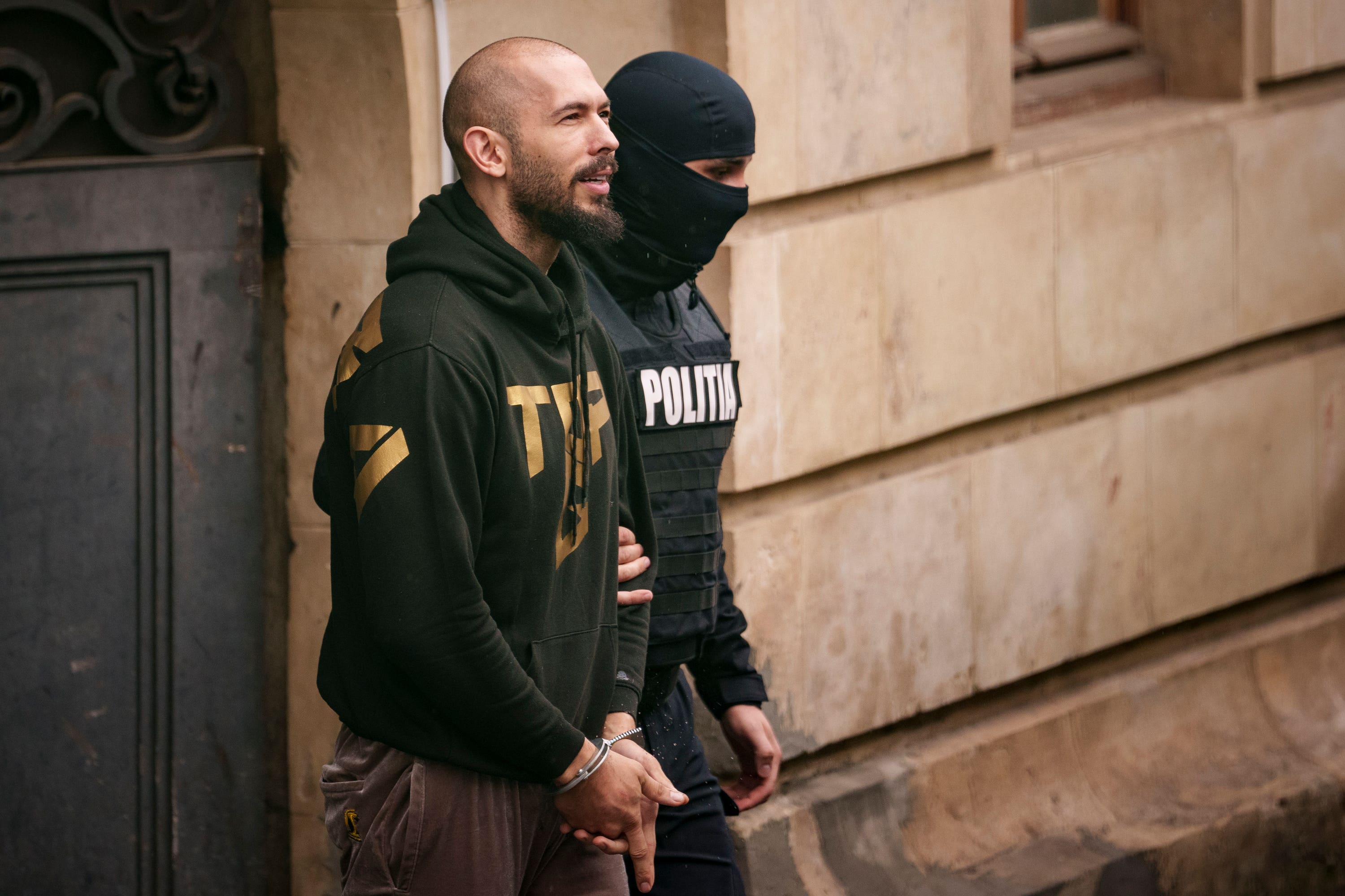 A police officer escorts Andrew Tate from the Court of Appeal in Bucharest.