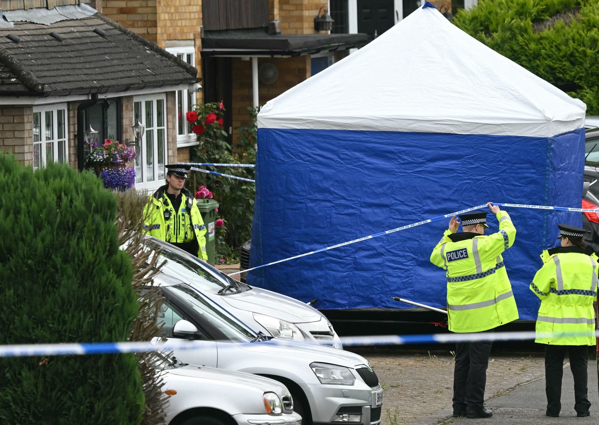 Police officers stand guard by a forensic team tent at Ashley Close in Bushey in the borough of Hertfordshire, north of London, on July 10, 2024 after a triple 'crossbow attack' murder.