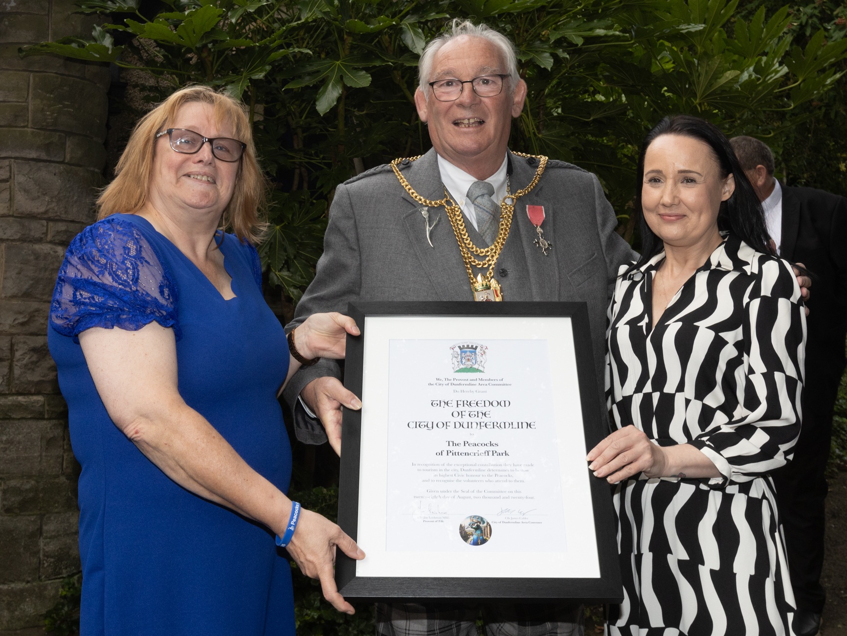 Provost Leishman presenting scroll to Suzi Ross and Carlyn Cane from Peacocks in Pittencrieff Park