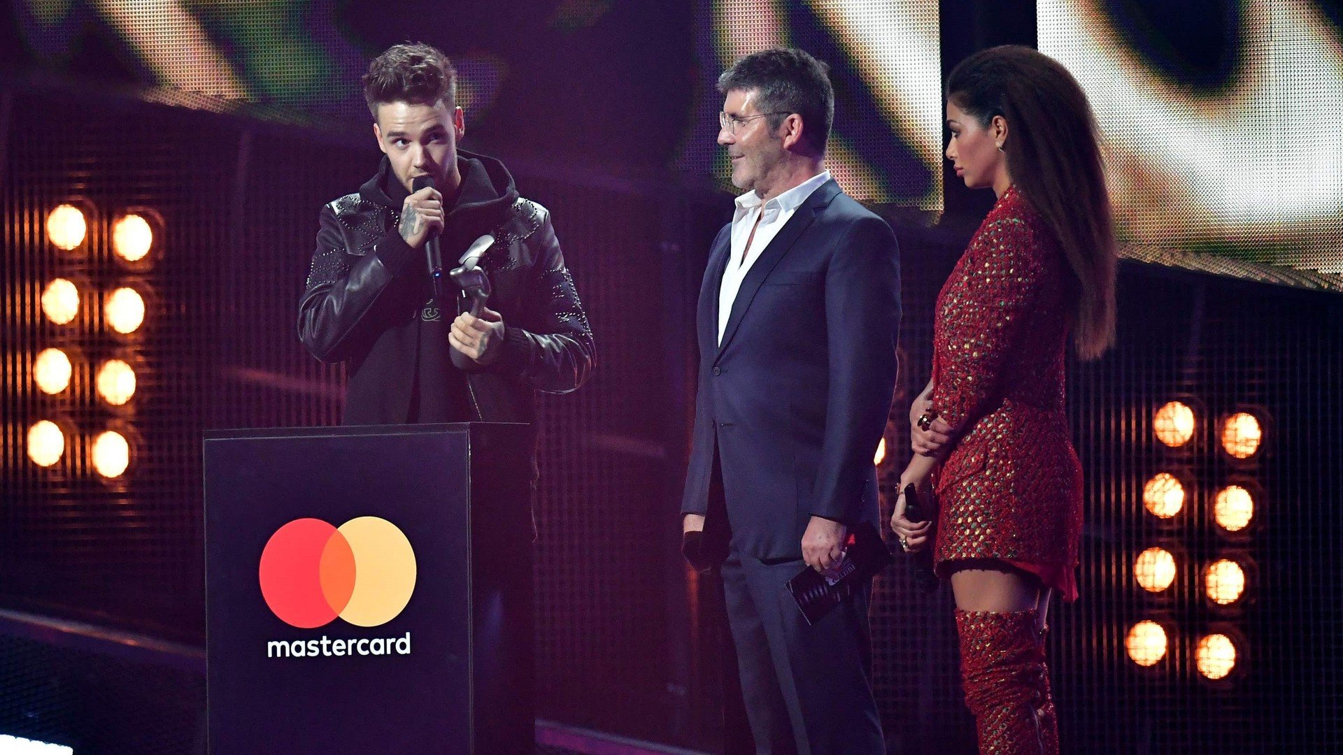 Nicole Scherzinger and Simon Cowell look on as Liam Payne collects his award for One Direction on stage at the Brit Awards 