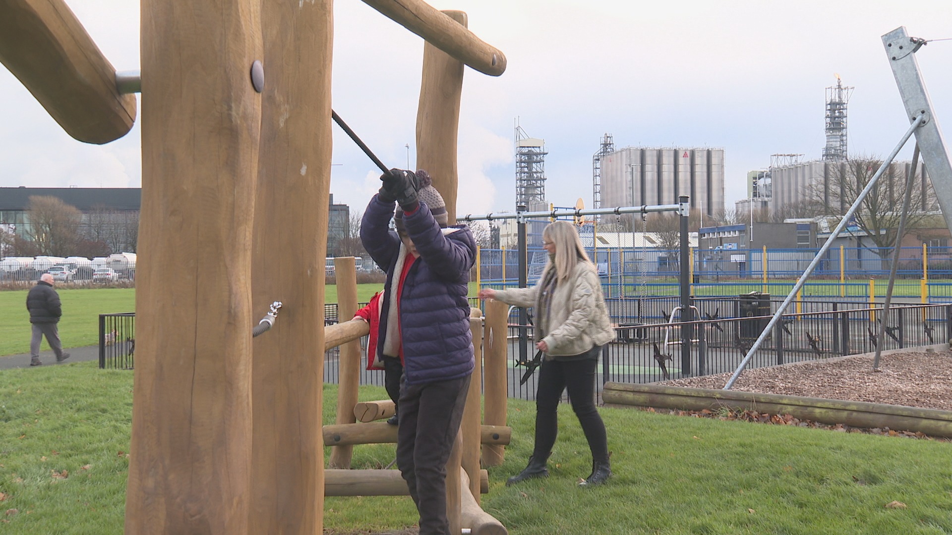 Fiona Binnie at a playpark with her children, Grangemouth oil refinery in background.