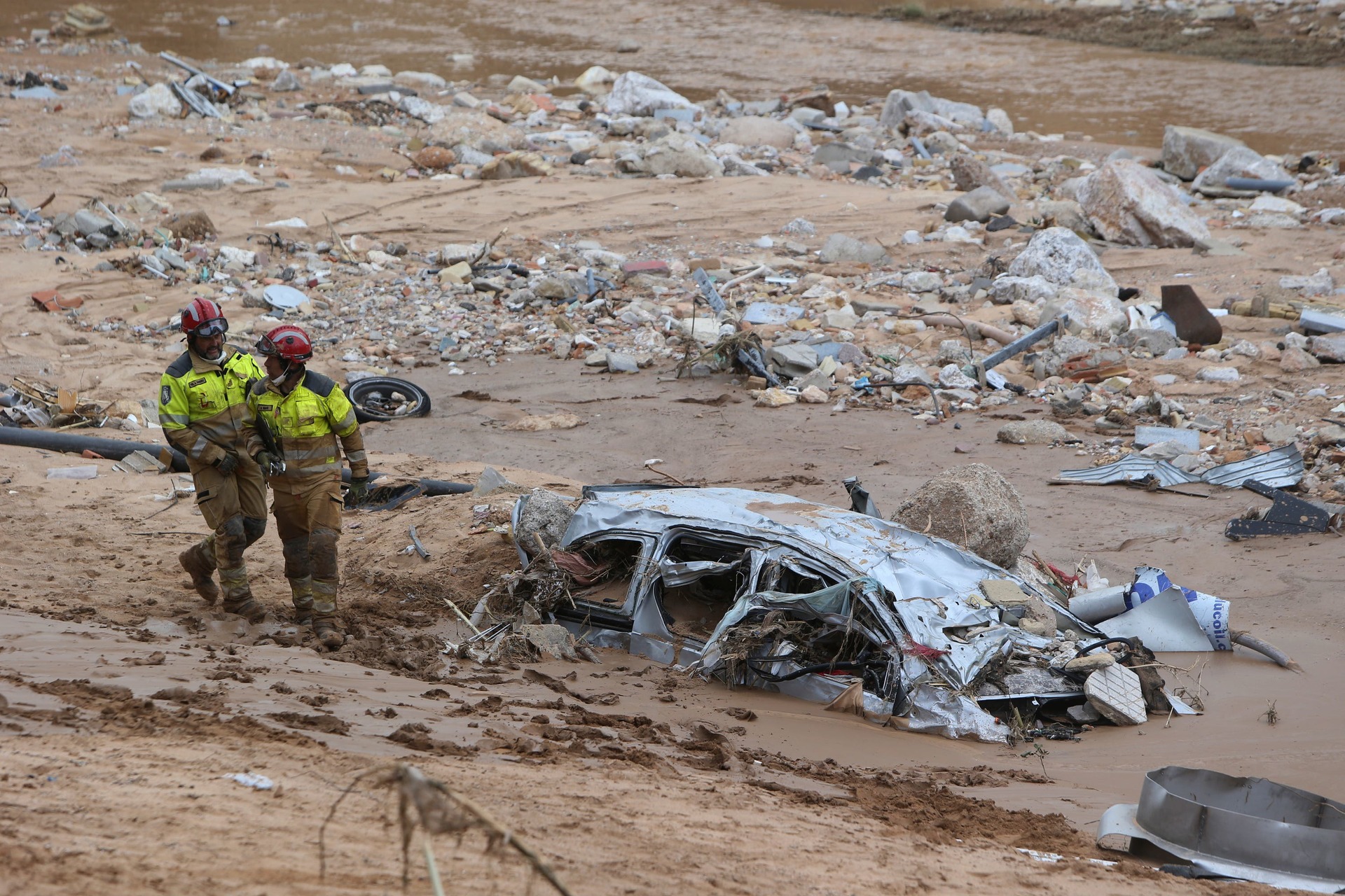 Rescue workers pass a car half-buried in mud after floods in Paiporta, near Valencia, Spain (Hugo Torres/AP) 