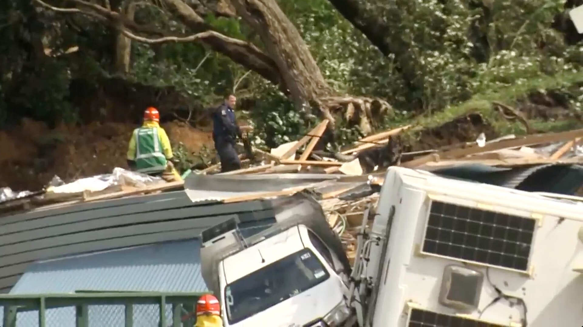 A police officer with a dog searches near the site of a landslide at the base of Mount Maunganui.