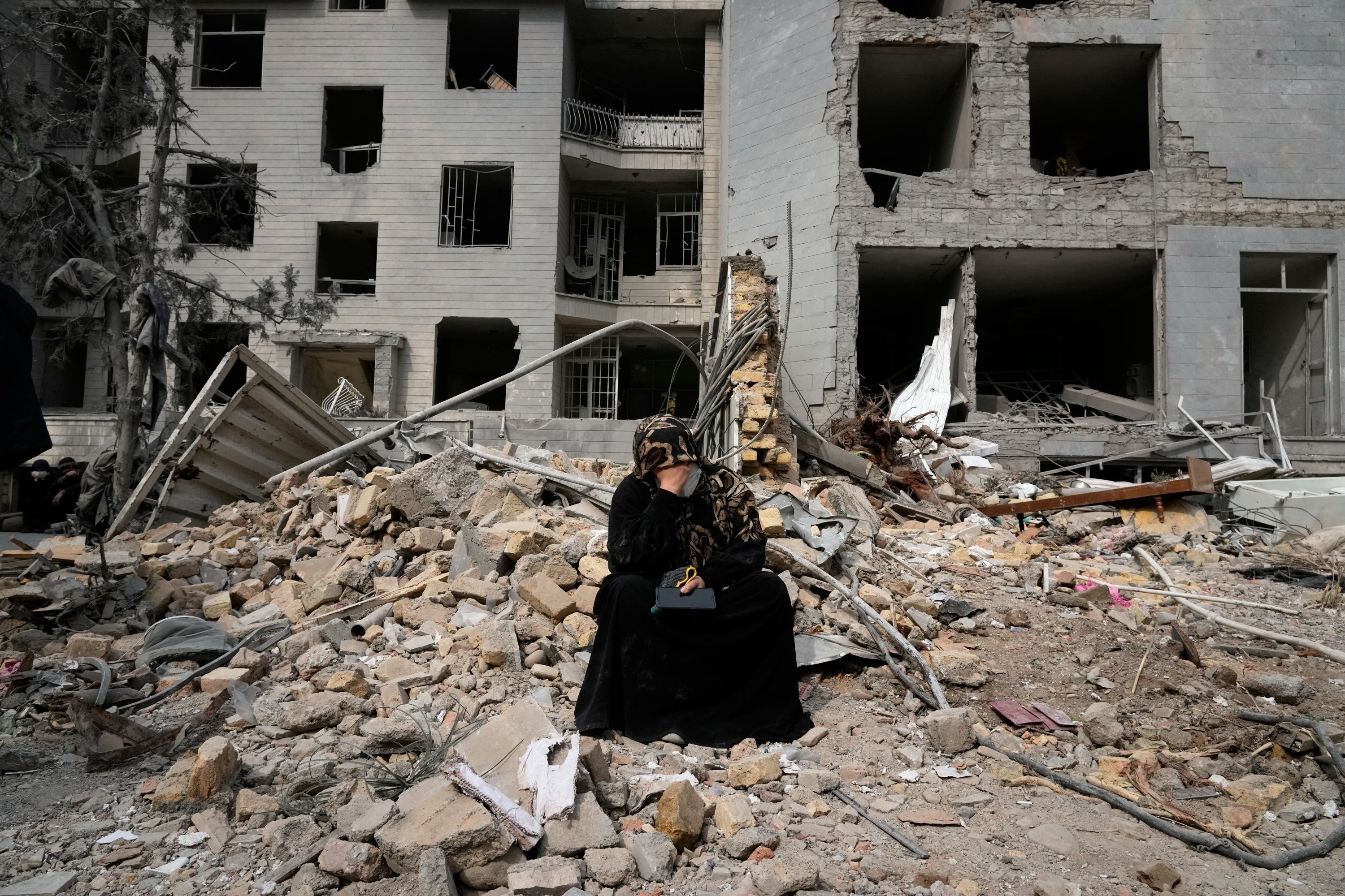 A woman sits on rubble across from a residential building damaged during a US-Israeli air campaign in Tehran, Iran.